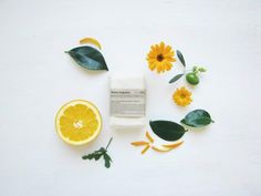 orange slices, leaves and soap on a white surface with flowers around the top half