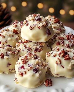 a white plate topped with cookies covered in frosting and chopped pecans next to a christmas tree