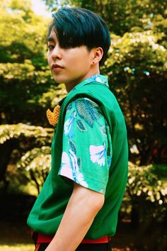 a young boy wearing a green shirt and red shorts standing in front of some trees