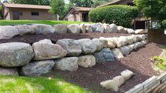 a rock wall in the middle of a yard with mulch and grass around it