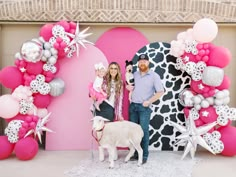 a man and two women standing in front of a pink backdrop with animals, balloons and stars