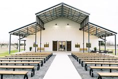 rows of wooden benches in front of a white building with black metal roof and windows