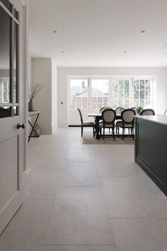 an open kitchen and dining room area with white walls, tile flooring and large windows