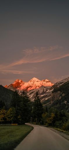 the sun is setting on a mountain range with trees and grass in front of it