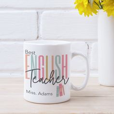 a white coffee mug with the words best english teacher on it next to a yellow flower