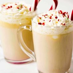 two mugs with hot chocolate and whipped cream in them, decorated with candy canes