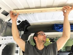 a man holding up a piece of wood in the back of a van