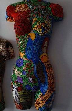 a body painted with many different colors and patterns, next to an object that looks like a mannequin