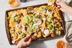 two hands reaching for an enchilada on a baking tray with drinks and condiments