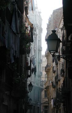 an alley way with clothes hanging from the buildings and street lamps on either side,