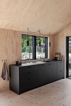 a kitchen with black cabinets and windows in the wall next to sliding glass doors that look out onto a wooded area