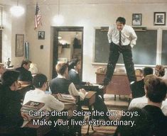 a man standing on top of a desk in front of a classroom full of people