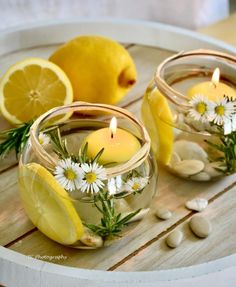 two lemons and some white flowers are in small glass bowls with candles on a wooden table