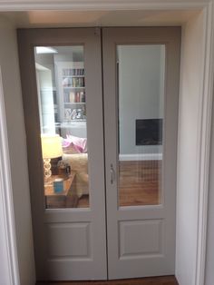 two glass doors in the corner of a room with hardwood floors and white paint on the walls