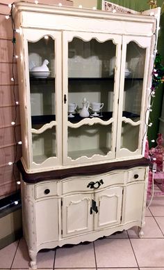 a white china cabinet with glass doors and lights on the wall behind it in a room