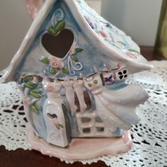 a ceramic birdhouse on a doily with a heart in the roof and flowers