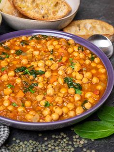 a purple bowl filled with chickpeas and spinach next to some bread slices