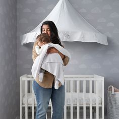 a woman holding a baby in her arms while standing next to a white crib