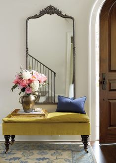 a yellow bench sitting in front of a mirror on top of a wooden floor next to a vase filled with flowers