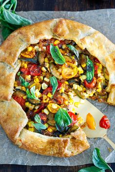 a vegetable pie with a slice missing from it on a piece of wax paper next to some leaves