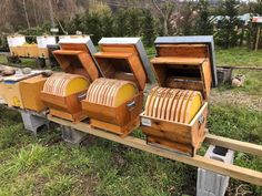 several beehives sitting on top of a wooden rail in the grass next to trees