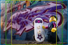 a lego figure holding a skateboard in front of a wall with graffiti on it