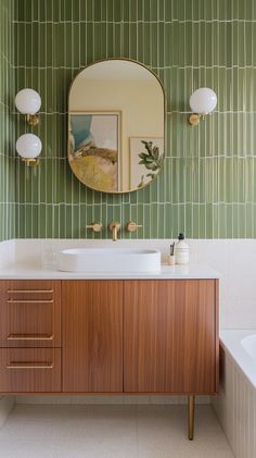 Elegant mid-century modern bathroom with Blu Dot-inspired elements, featuring a freestanding vanity in walnut wood with tapered legs and flat-front doors with brass pull handles, reminiscent of classic mid-century furniture. The countertop is a white quartz slab, paired with a modern, curved brass faucet for a touch of vintage charm. The bathtub area is wrapped in olive green subway tiles with a glossy finish, arranged in a stacked pattern to add a contemporary edge. Above the vanity, an arched mirror with a thick brass frame makes a statement, flanked by retro-inspired sconces with globe bulbs and brass accents. The floor is laid with terrazzo tiles in shades of cream and beige, adding texture and visual interest, while framed vintage artwork on the walls completes the space with a refine Bathroom Tile Mid Century Modern, Bathroom Decor Mid Century Modern, Vintage Inspired Bathroom Vanity, Mid Centric Modern Bathroom, Small Bathroom Ideas Mid Century Modern, Beach Modern Bathroom, Mid Century Tile Bathroom, Mid Century Bathrooms, Mid Century Modern Half Bath