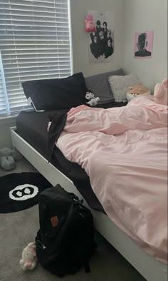 a bed with pink sheets and pillows in a bedroom next to a black duffle bag