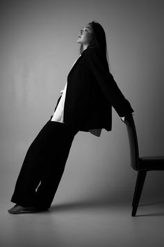 a woman sitting on top of a chair in front of a gray wall with her legs spread out