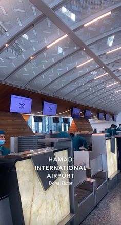 the interior of an airport with people sitting at their desks and television screens above them