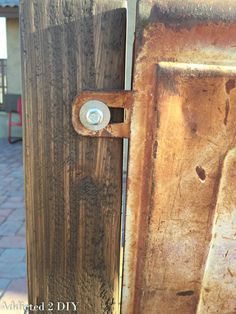 an old wooden door with a rusted metal latch on it's side and brick walkway in the background