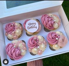 a box filled with pink and white cupcakes on top of a green field