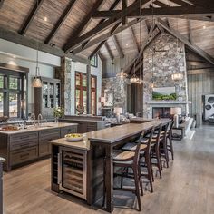 a large open concept kitchen and living room with wood flooring, exposed beams, stone fireplace, and vaulted ceiling