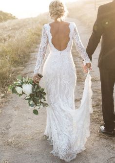 a bride and groom holding hands walking down a dirt road in front of the sun