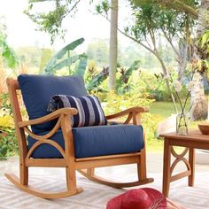 a rocking chair with pillows and a hat on the floor in front of a tree