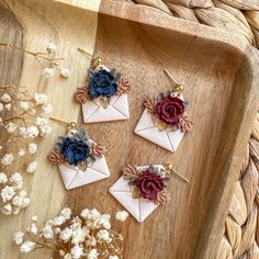 four small white envelopes with flowers on them sitting on a wooden tray next to dried flowers