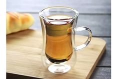 a glass cup filled with liquid sitting on top of a cutting board next to bread