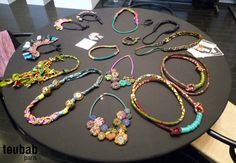 a table topped with lots of different colored necklaces on top of a black table