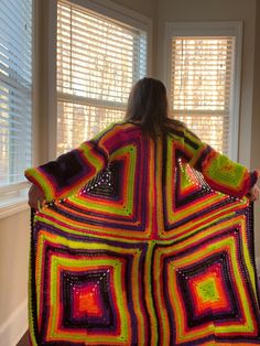 a woman holding up a crocheted blanket in front of a window with shutters