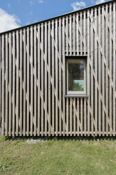 the side of a wooden building with a window and grass area in front of it