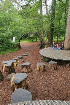 people are sitting on benches made out of logs in the woods near a wooden walkway