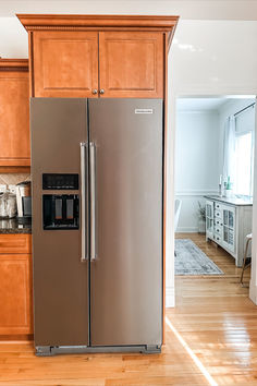 a stainless steel refrigerator in the middle of a kitchen with wooden cabinets and hardwood floors