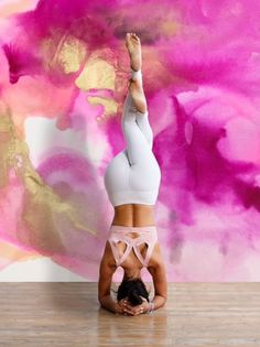 a woman is doing a handstand in front of a pink and gold background