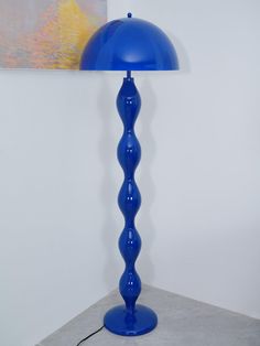 a blue lamp sitting on top of a table next to a painting and a wall