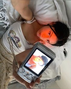 a woman laying in bed while holding an old style video game console with her face painted orange