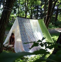 a woman sitting in front of a green and white tarp next to trees on the ground