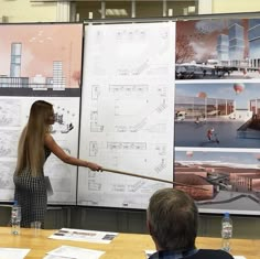 a woman pointing to a wall with drawings on it and people sitting at a table