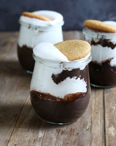 three jars filled with chocolate and marshmallows on top of a wooden table