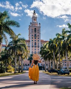 a woman in a yellow dress and straw hat walks down the street near palm trees