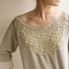 a woman wearing a gray sweater with yellow squares on the front and back of her shirt